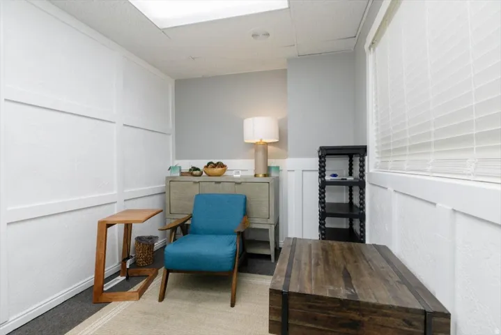 Living area with a decorative wall, light colored carpet, a drop ceiling, and wainscoting