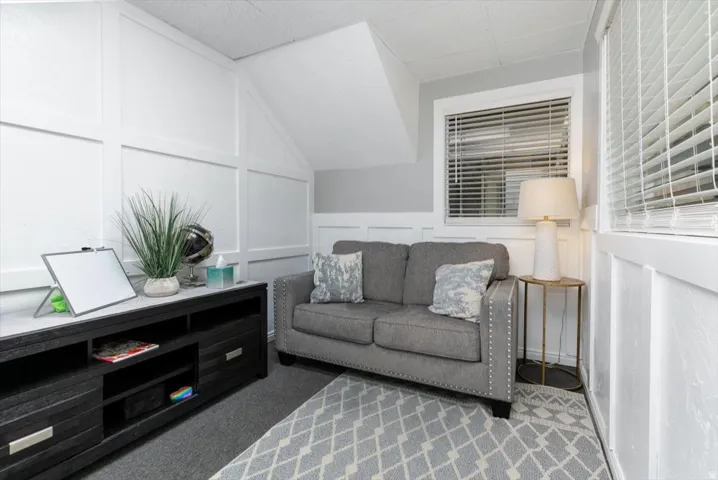 Living area with a decorative wall, vaulted ceiling, and carpet floors