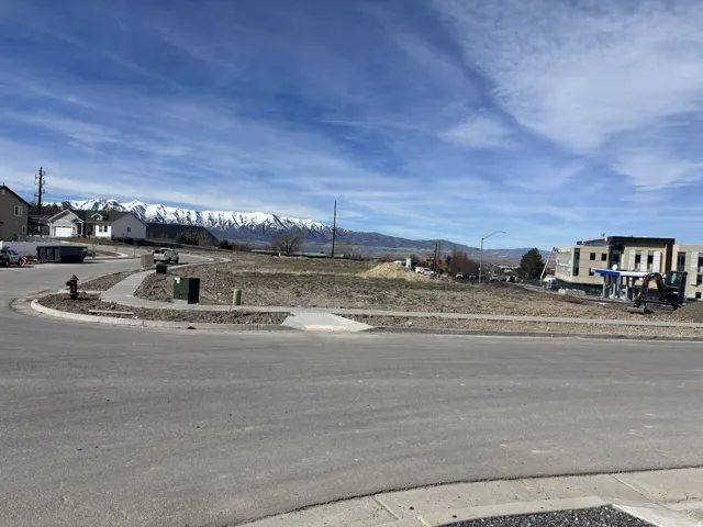 View of asphalt road with sidewalks, curbs, a mountain view, and street lighting