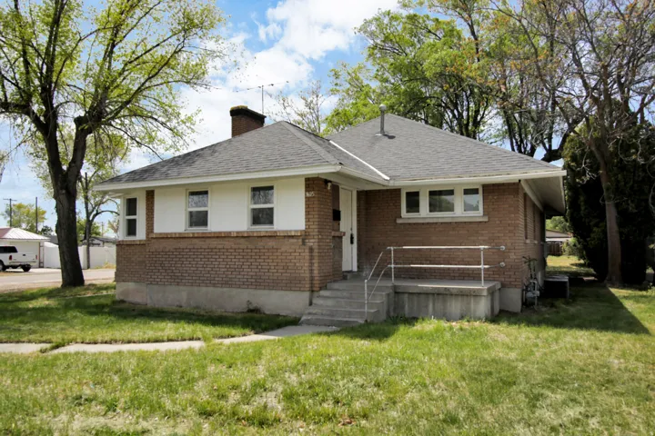 View of front of house with brick siding, a front lawn, a chimney, and roof with shingles