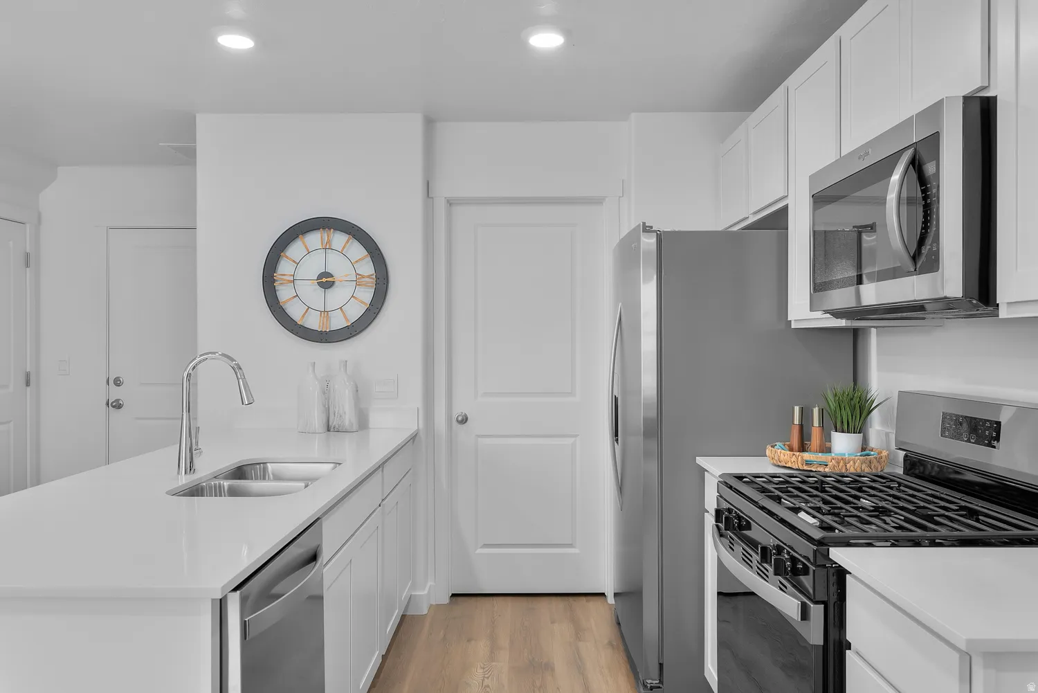 Kitchen featuring stainless steel appliances, a peninsula, white cabinetry, light stone counters, and light wood-style flooring