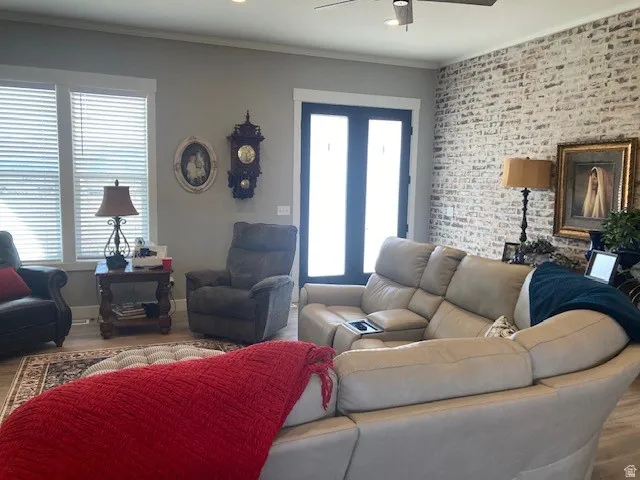 Living area featuring wood finished floors, brick wall, ornamental molding, ceiling fan, and an accent wall