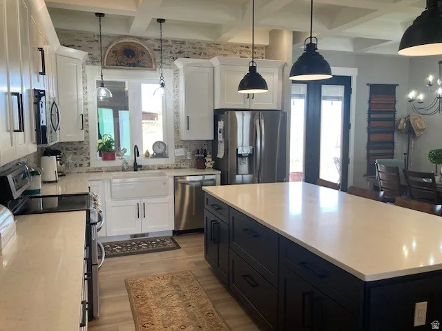 Two tone kitchen with two tone color scheme, stainless steel appliances, coffered ceiling, light wood finished floors, and decorative backsplash