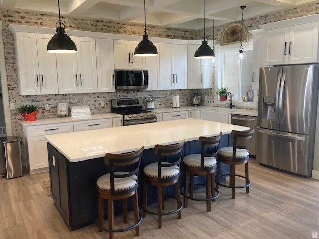 Kitchen with stainless steel appliances, a breakfast bar area, a center island, decorative light fixtures, and two tone color scheme