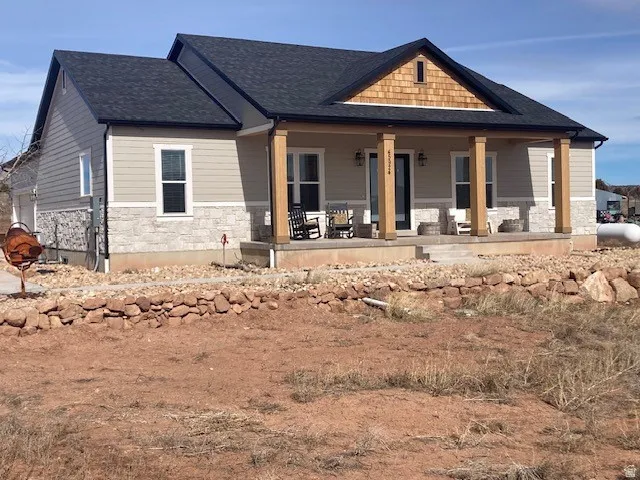 View of front of property with stone siding, a porch, and a shingled roof