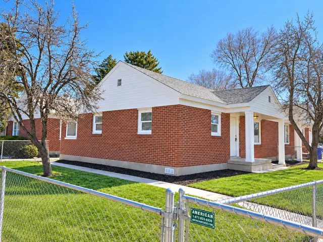 Brick exterior with white trim, covered front porch, concrete pathway, and a chain link fence