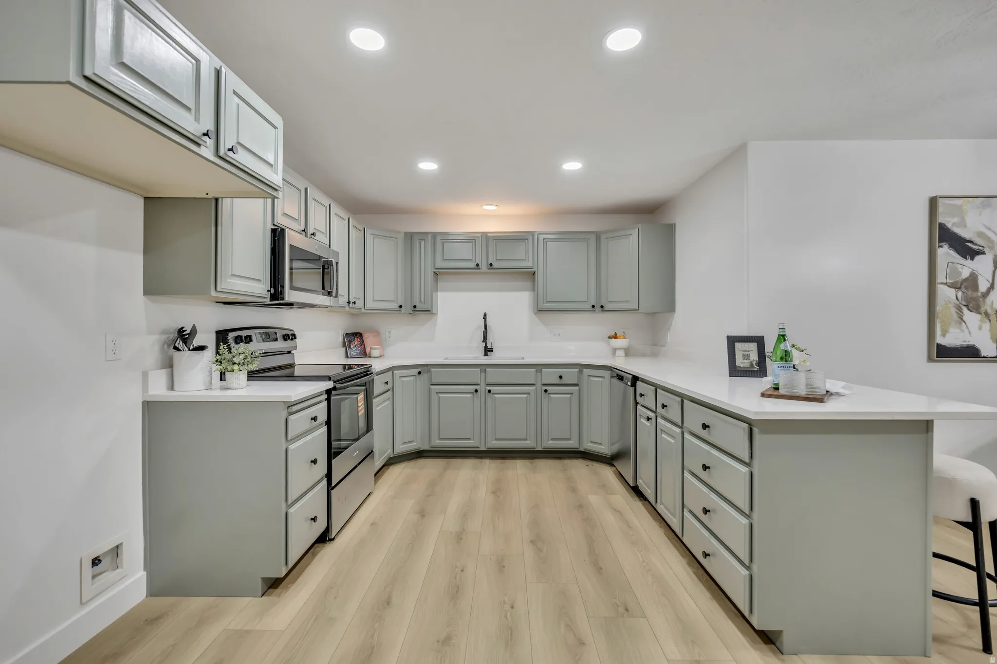 Kitchen with a peninsula, stainless steel appliances, light wood-style flooring, a breakfast bar, and light countertops