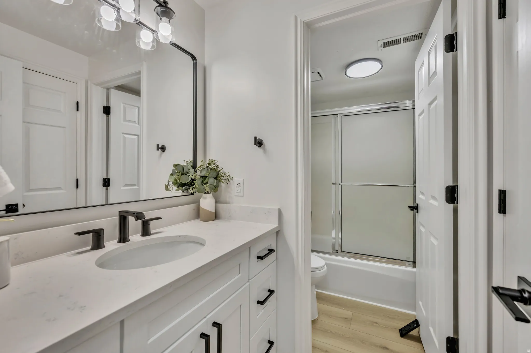 Bathroom featuring vanity, bath / shower combo with glass door, and light wood-style flooring