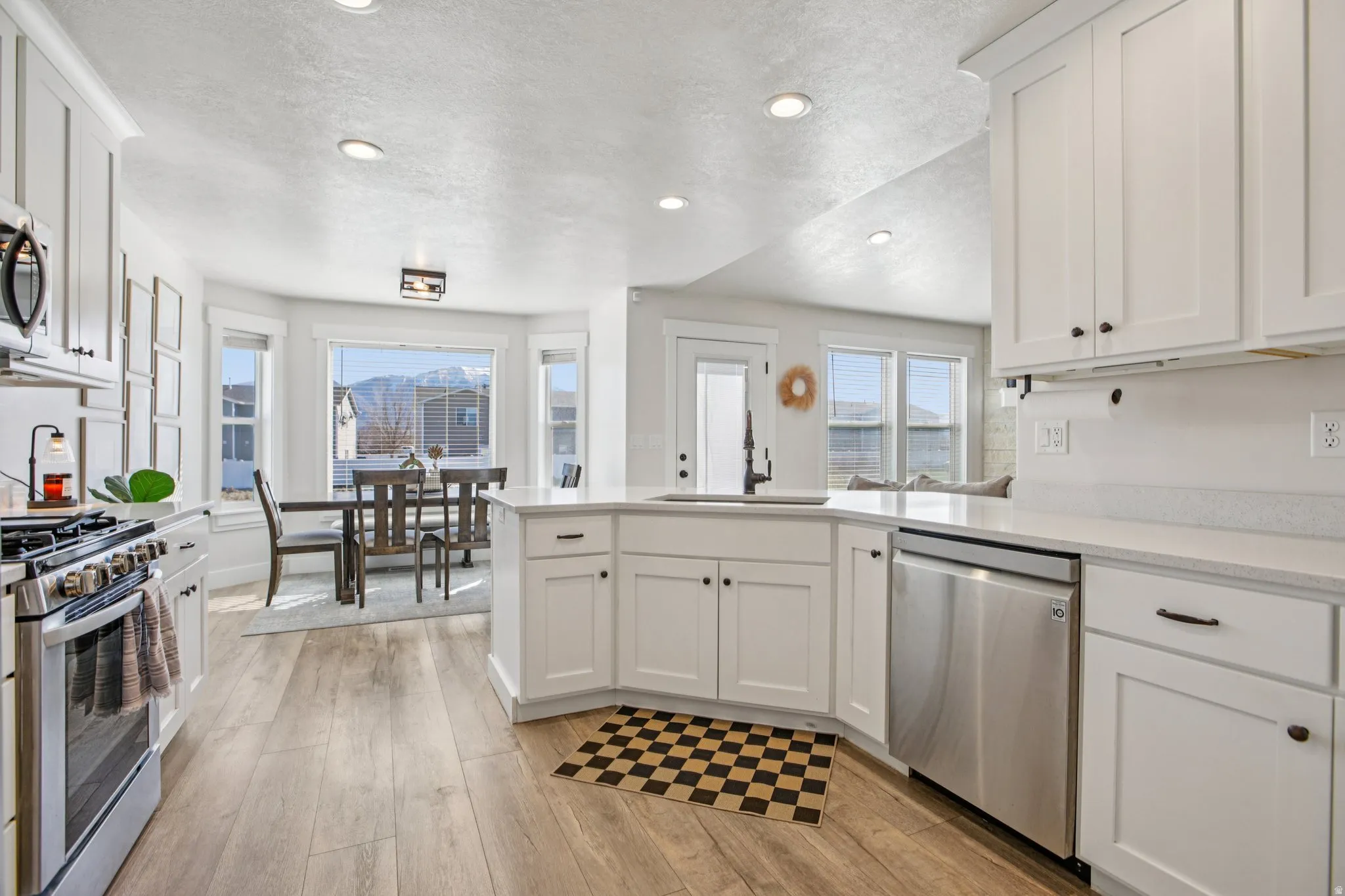 Kitchen with a peninsula, white cabinetry, stainless steel appliances, light wood-type flooring, and a textured ceiling