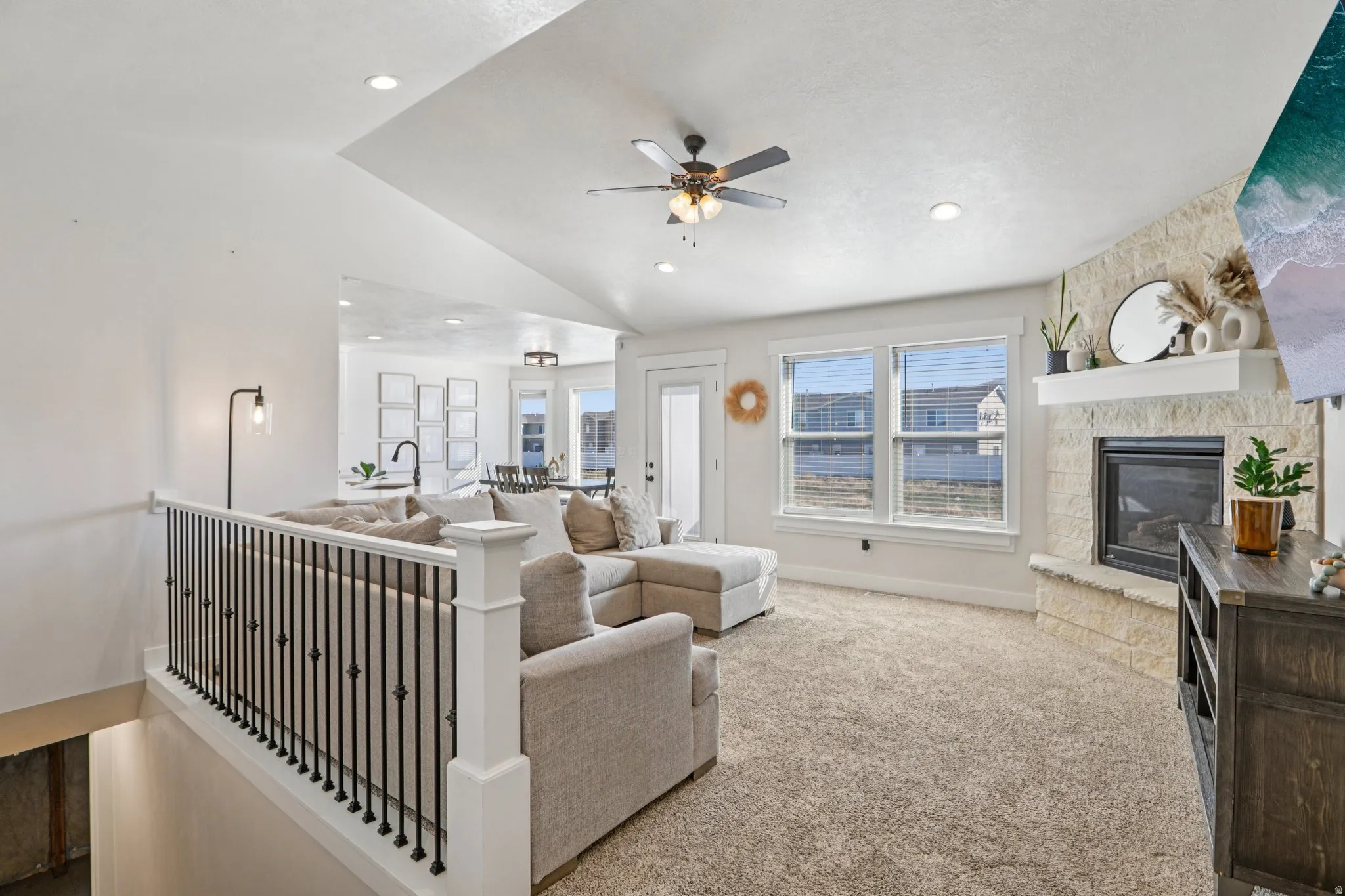 Living room featuring a ceiling fan, vaulted ceiling, carpet, and a stone fireplace