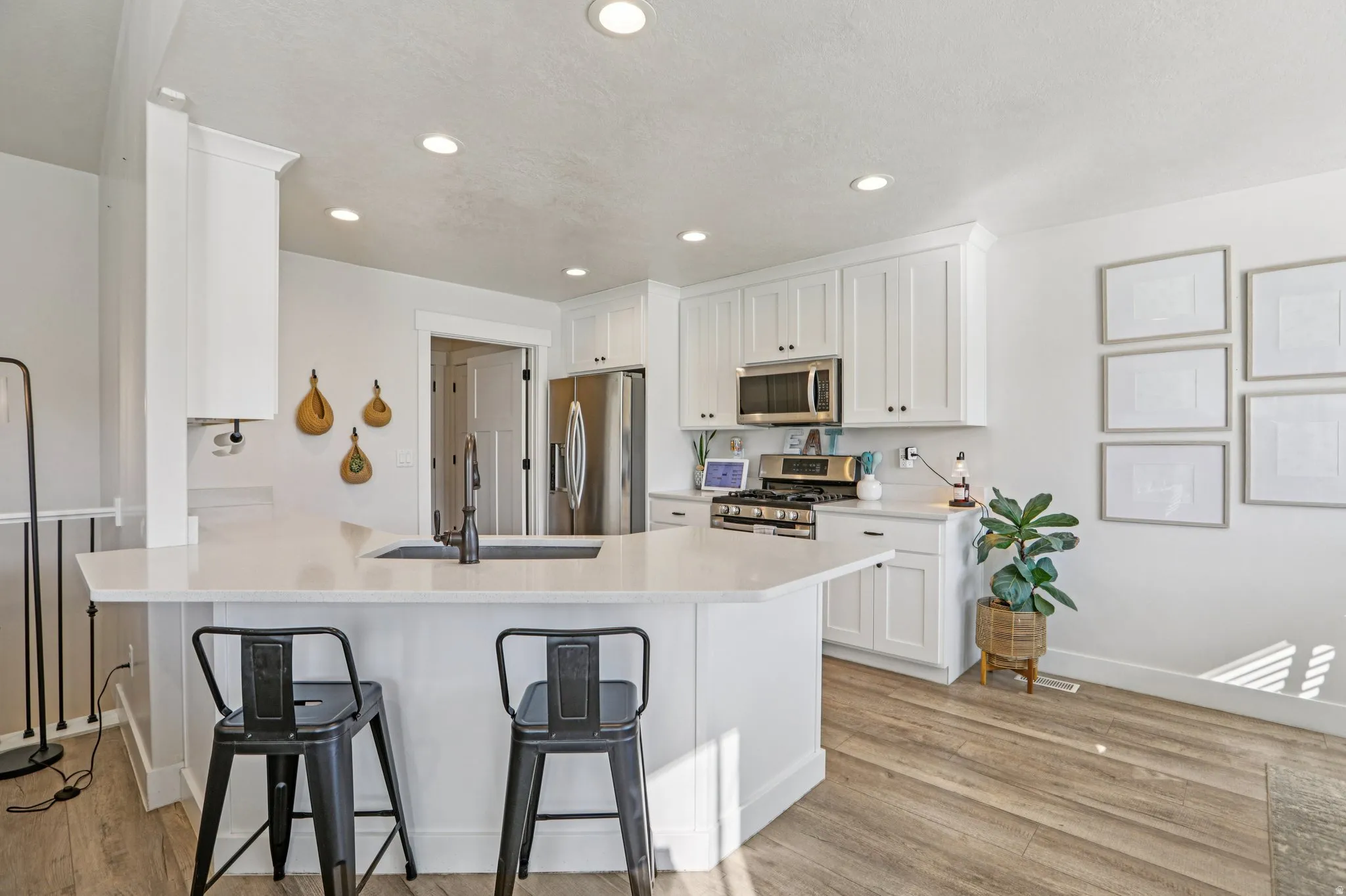 Kitchen with white cabinets, a peninsula, stainless steel appliances, a breakfast bar, and light wood-type flooring
