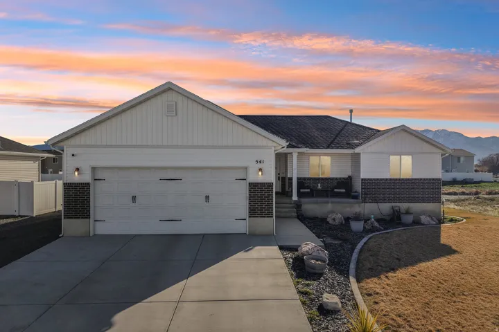 View of front of home with brick siding, driveway, an attached garage, and a porch
