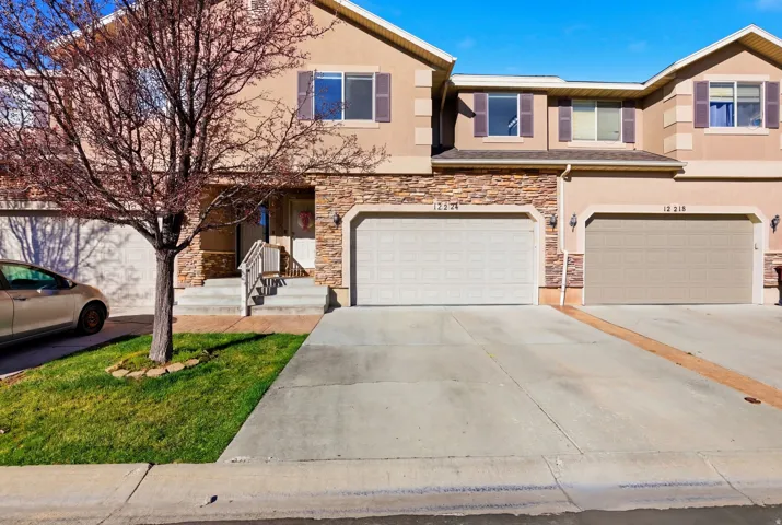 View of front of property with stucco siding, stone siding, a garage, and concrete driveway