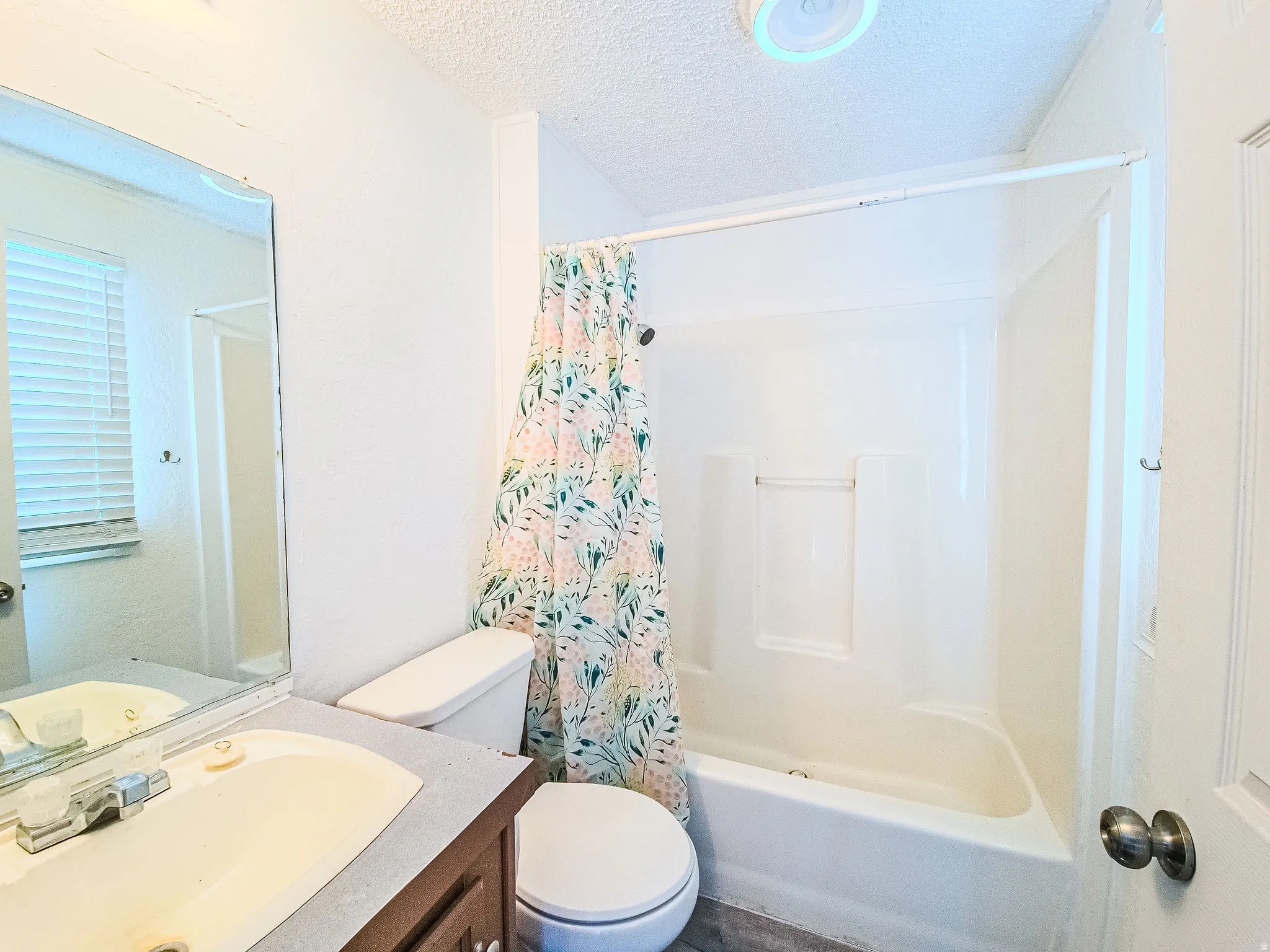 Full bathroom with a textured ceiling, vanity, and shower / tub combo with curtain