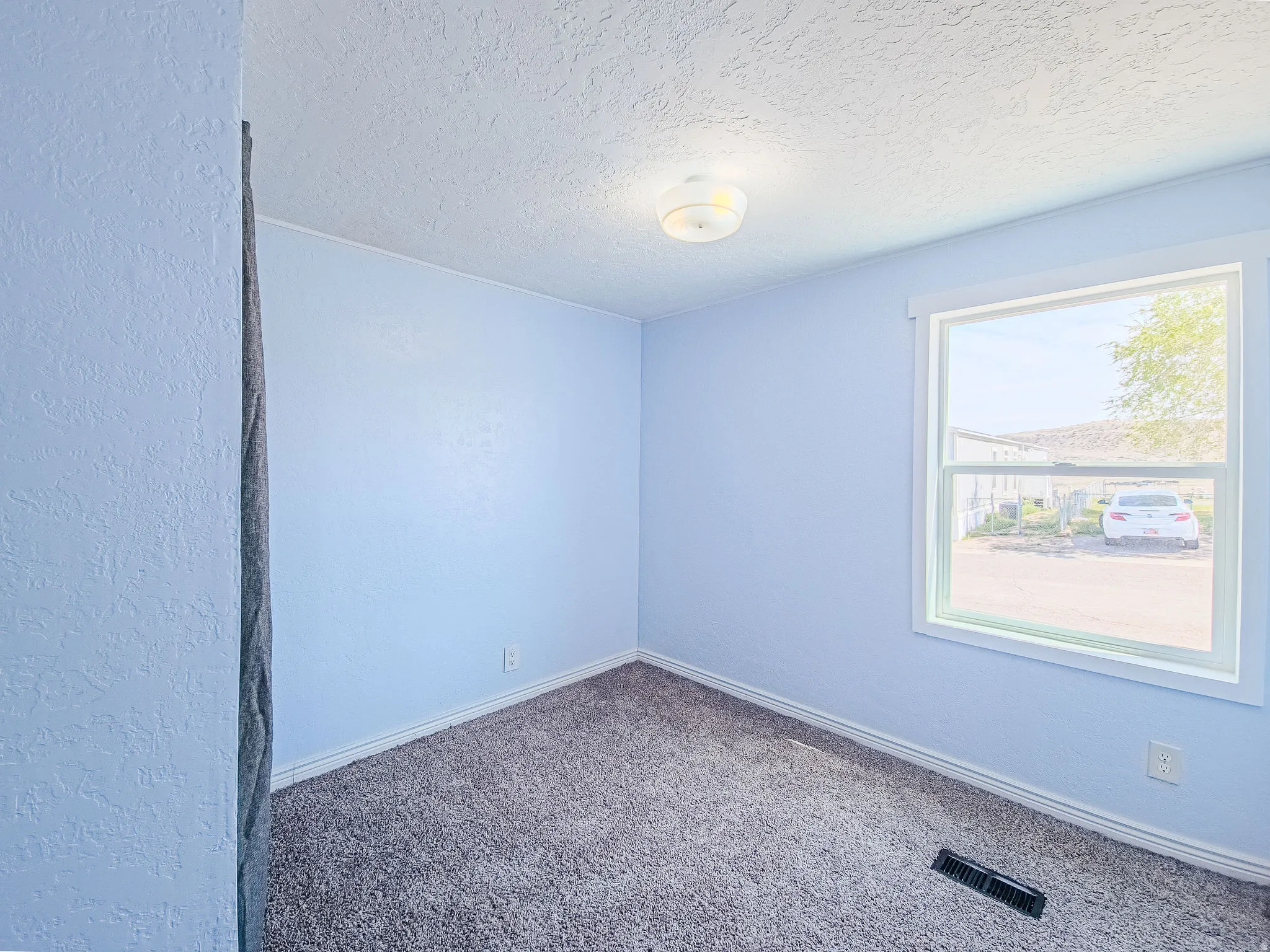 Carpeted empty room with a textured ceiling and baseboards