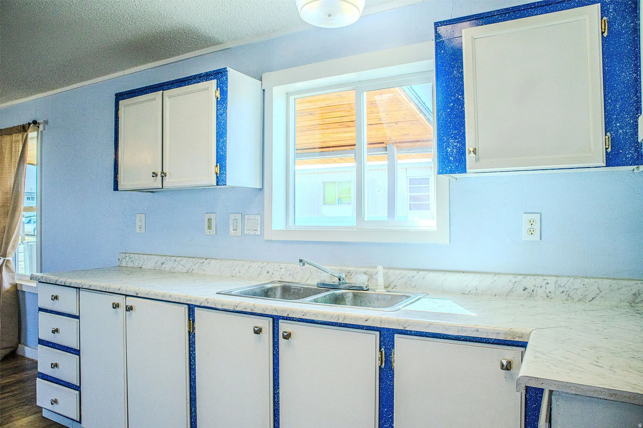Kitchen featuring healthy amount of natural light, light countertops, white cabinets, ornamental molding, and a textured ceiling