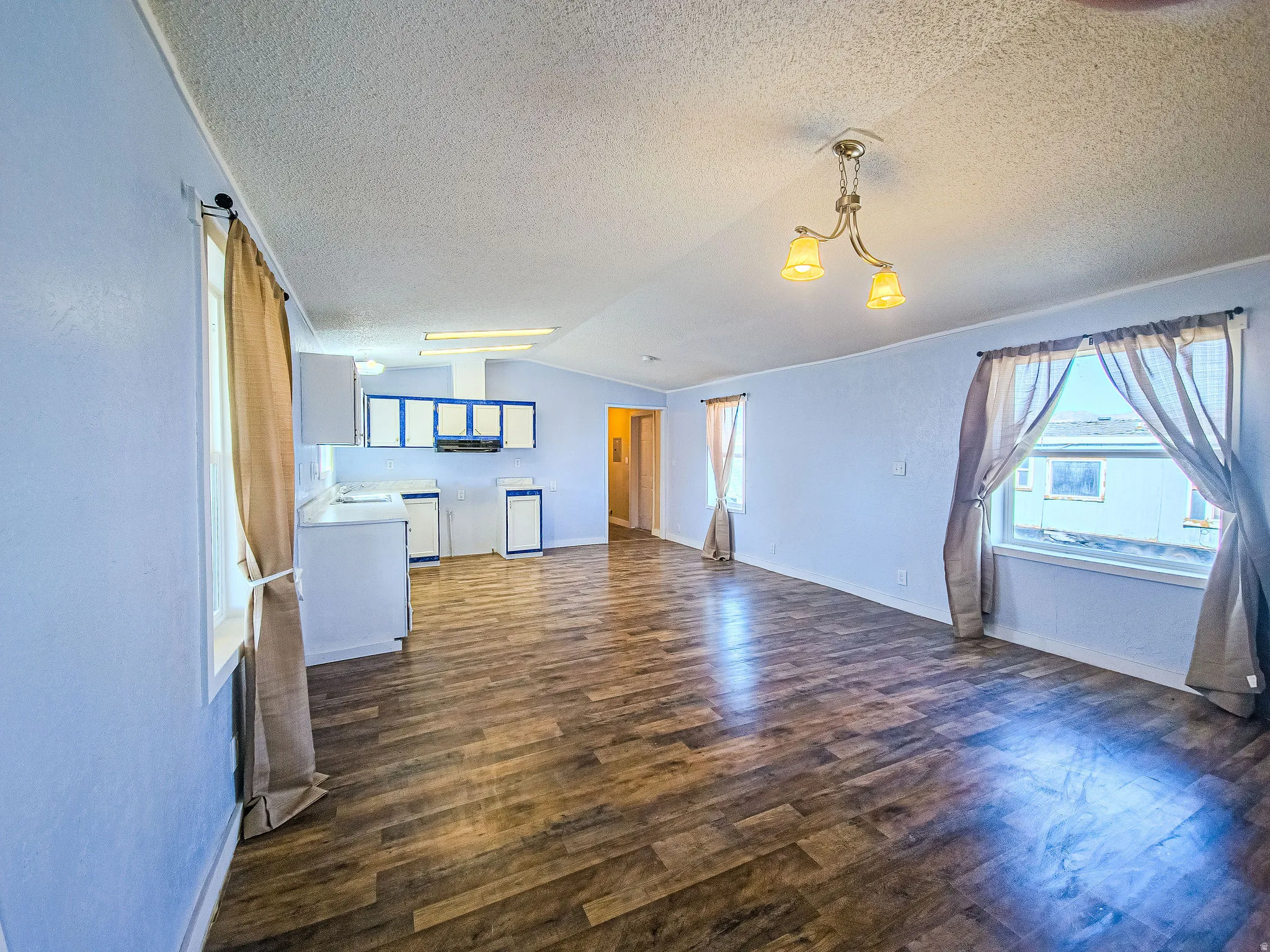 Unfurnished living room featuring dark wood-style flooring and baseboards