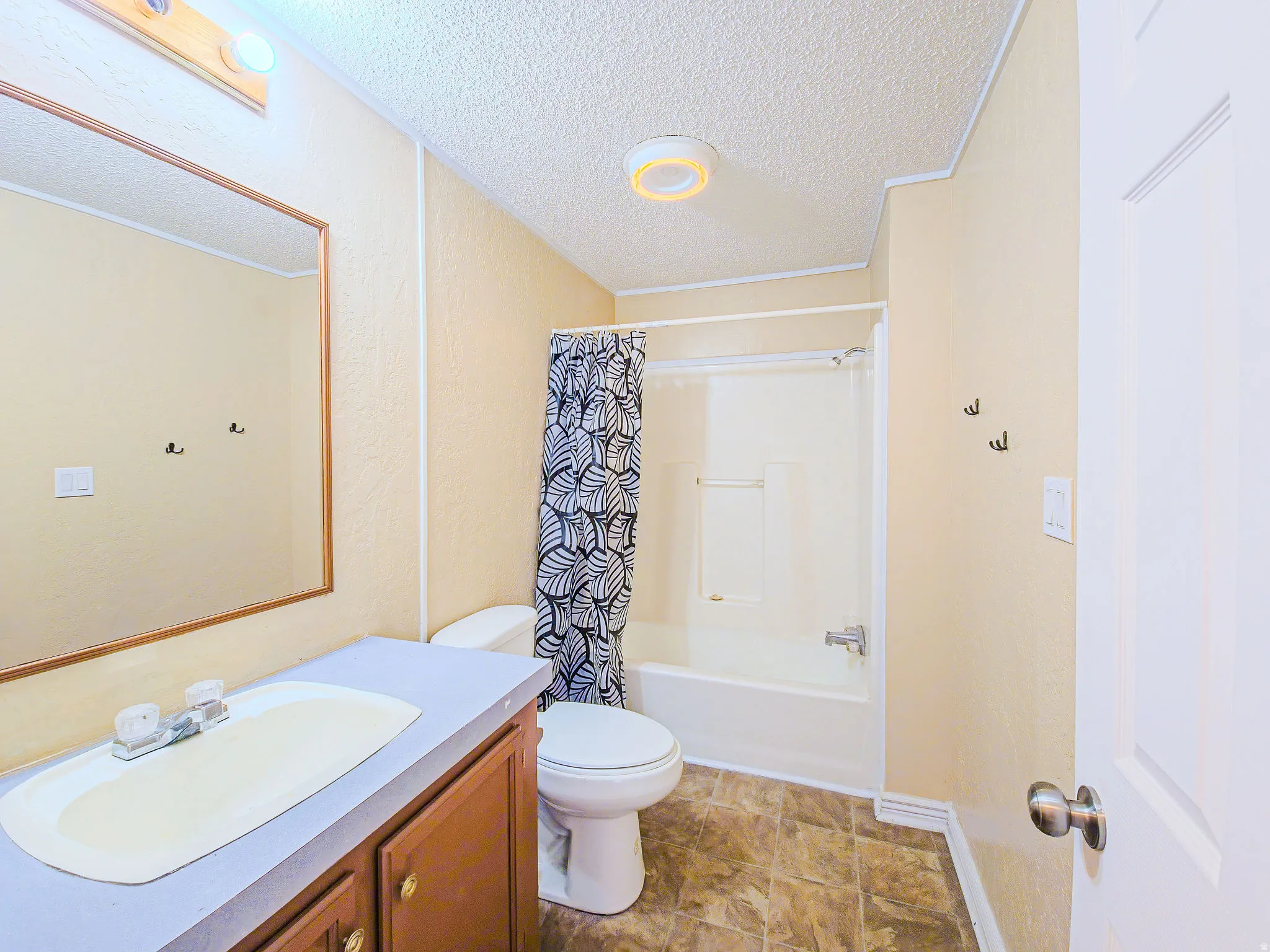 Bathroom featuring vanity, shower / bath combination with curtain, and a textured ceiling