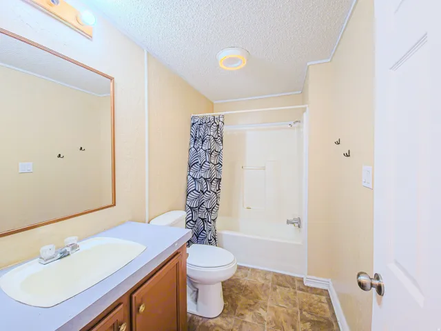 Bathroom featuring vanity, shower / bath combination with curtain, and a textured ceiling