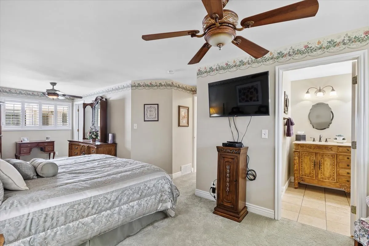 Bedroom featuring light carpet, a ceiling fan, and ensuite bathroom
