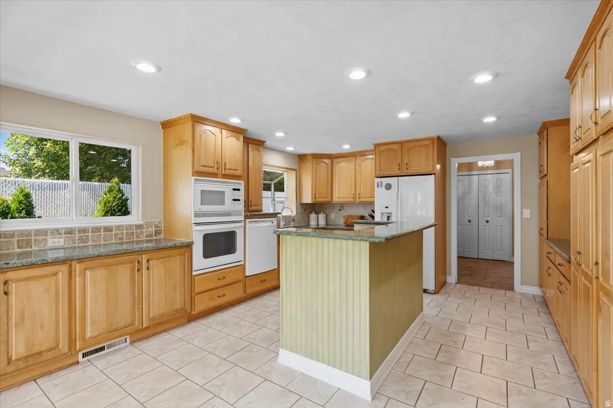 Kitchen featuring decorative backsplash, a kitchen island, white appliances, dark stone counters, and recessed lighting