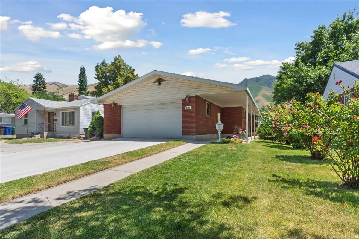 Single story home featuring a mountain view, concrete driveway, a front lawn, an attached garage, and brick siding