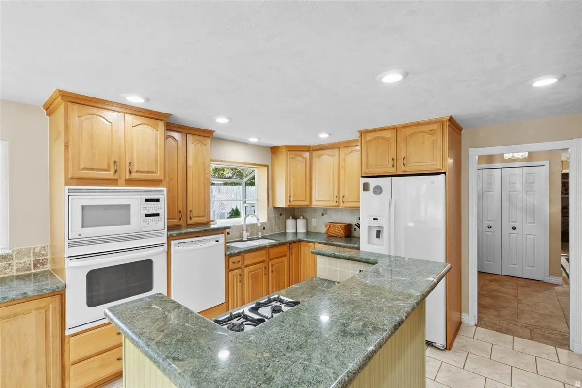 Kitchen featuring white appliances, a center island, backsplash, dark stone counters, and light tile patterned floors