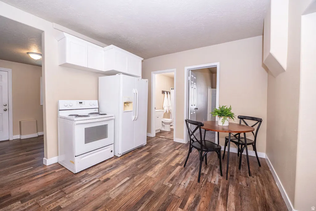 Kitchen with electric stove, dark wood-type flooring, white cabinets, and a textured ceiling