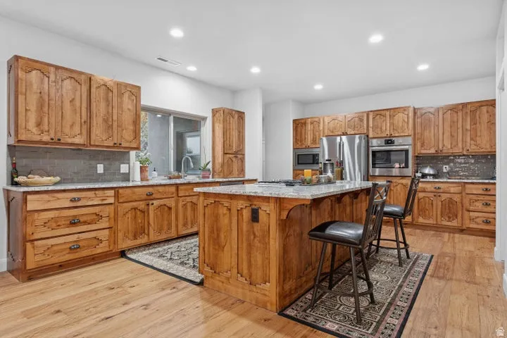 Kitchen with backsplash, wood finish cabinetry, light stone countertops, a kitchen island, and stainless steel appliances