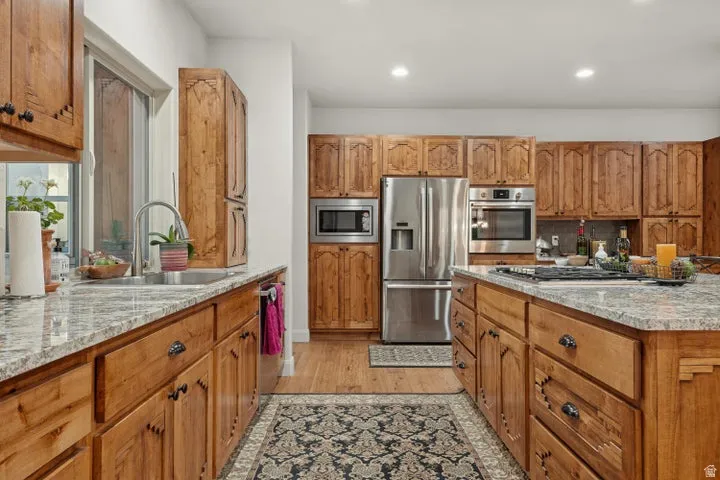 Kitchen featuring light stone countertops, wood finish cabinets, light wood finished floors, stainless steel appliances, and recessed lighting