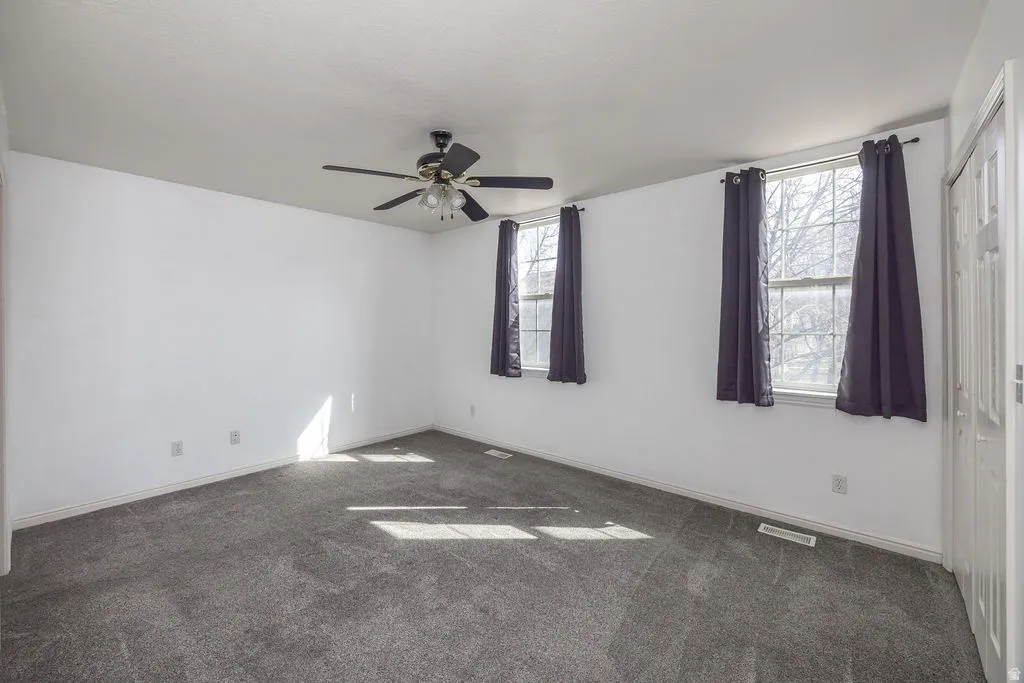 Carpeted empty room with a ceiling fan and baseboards