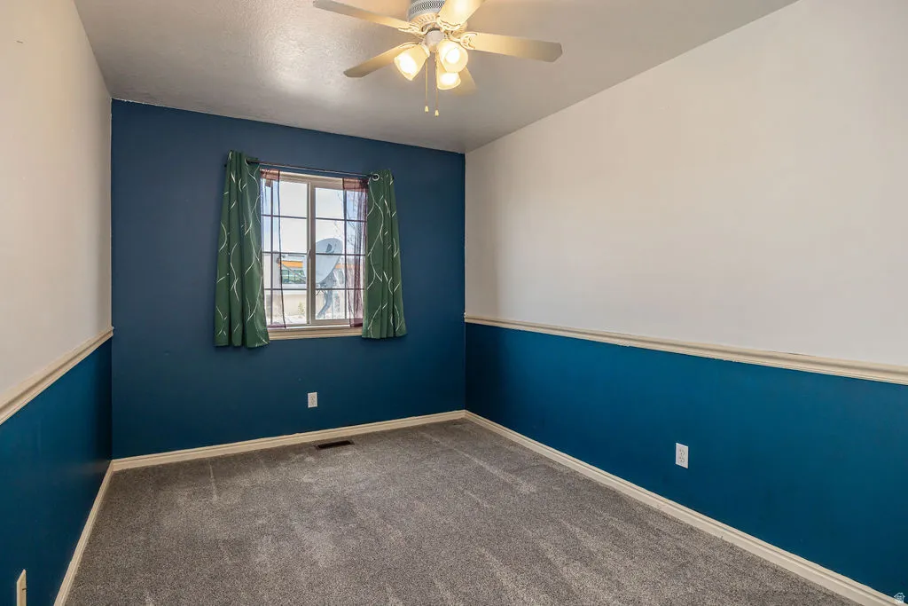Carpeted spare room featuring a ceiling fan and baseboards