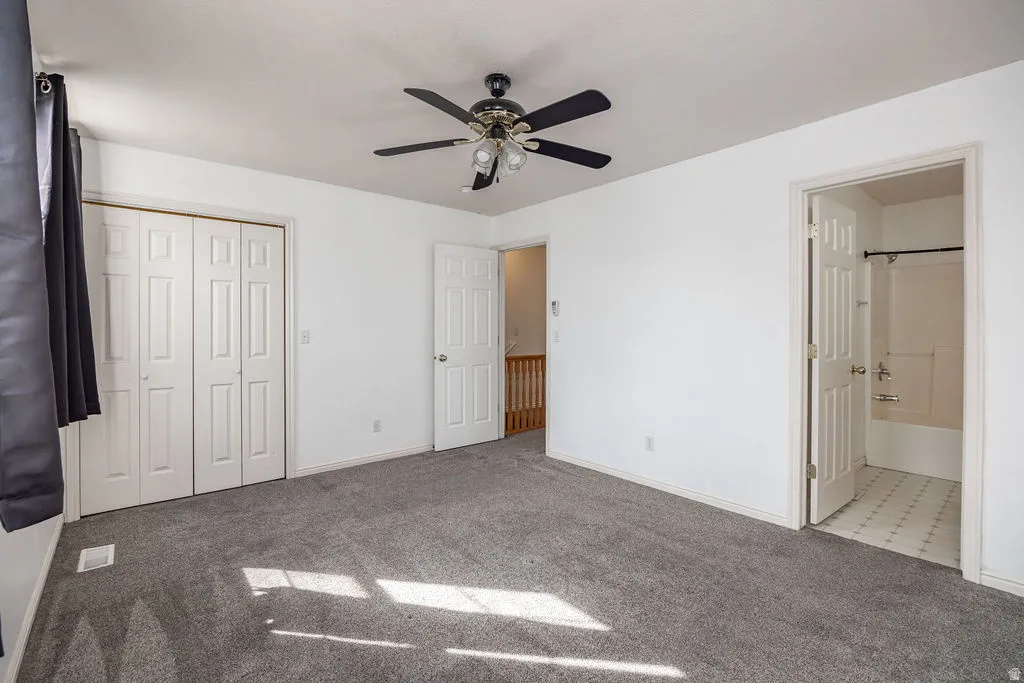 Unfurnished bedroom with light colored carpet, ceiling fan, ensuite bath, and a closet
