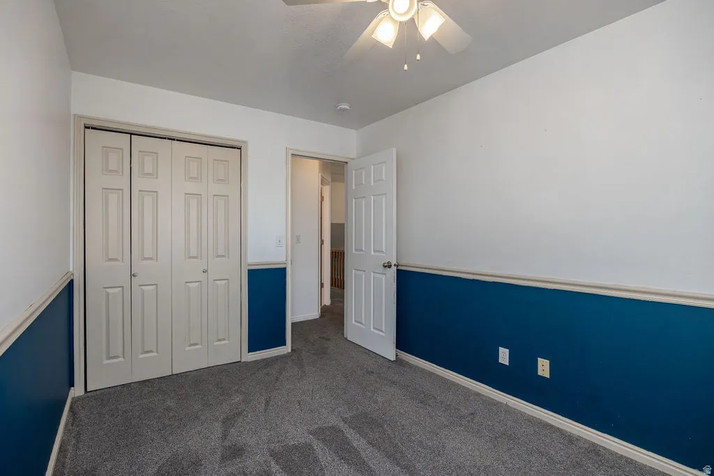Unfurnished bedroom with dark colored carpet, a ceiling fan, and a closet