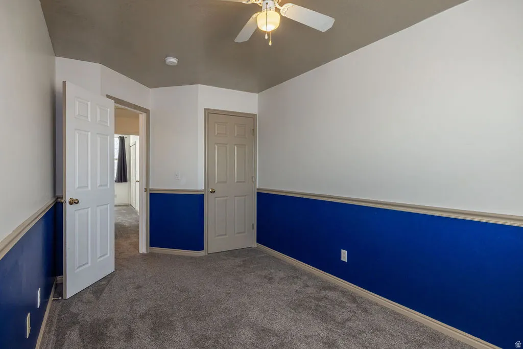 Unfurnished bedroom featuring dark carpet and ceiling fan