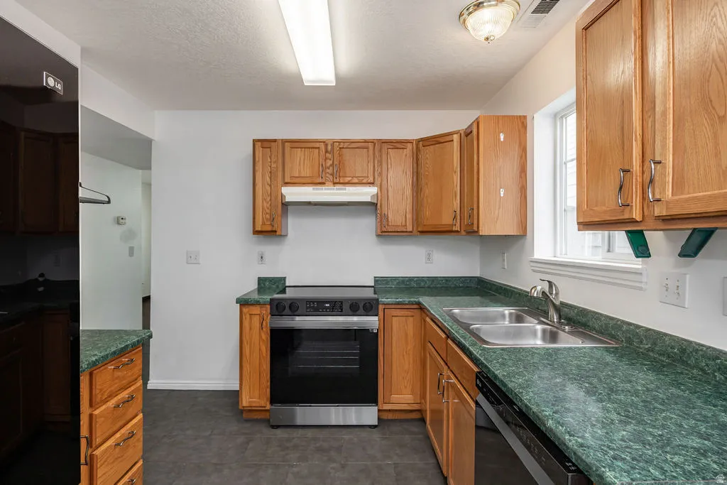 Kitchen with range with electric cooktop, dark countertops, wood finish cabinetry, and a textured ceiling