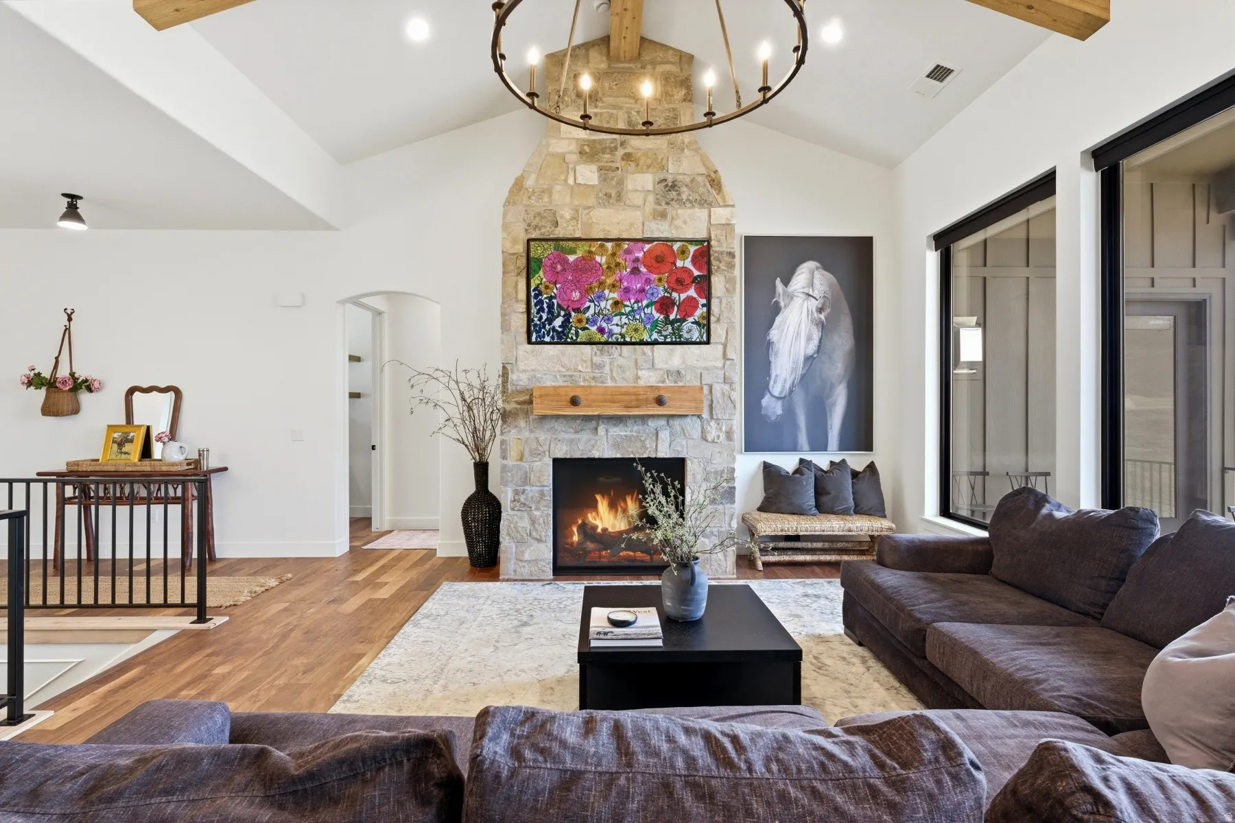 Living area featuring beamed ceiling, wood finished floors, a fireplace, arched walkways, and a chandelier