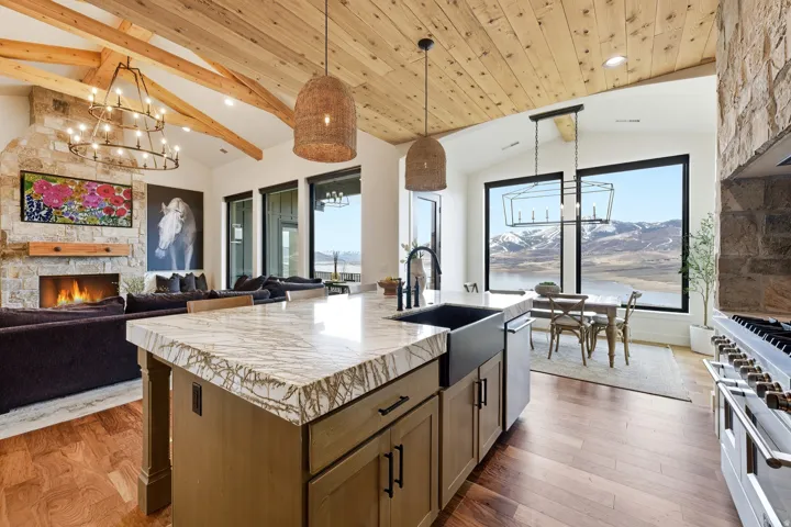 Kitchen with a chandelier, a kitchen island with sink, a stone fireplace, open floor plan, and stainless steel appliances