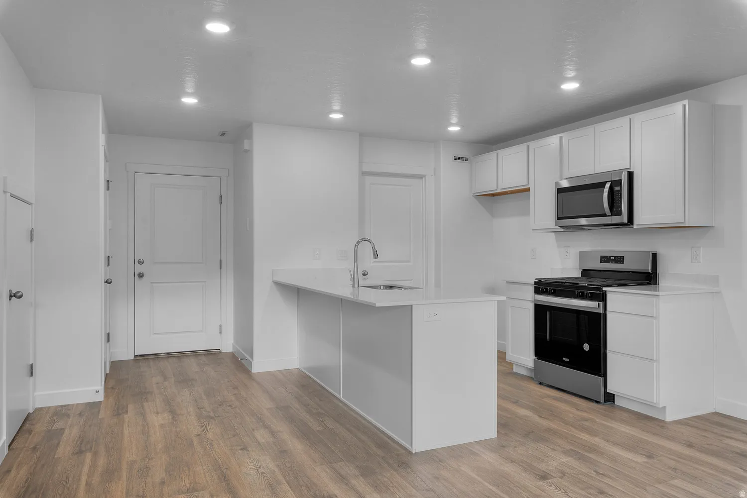 Kitchen with white cabinets, stainless steel appliances, a peninsula, light wood-style flooring, and recessed lighting