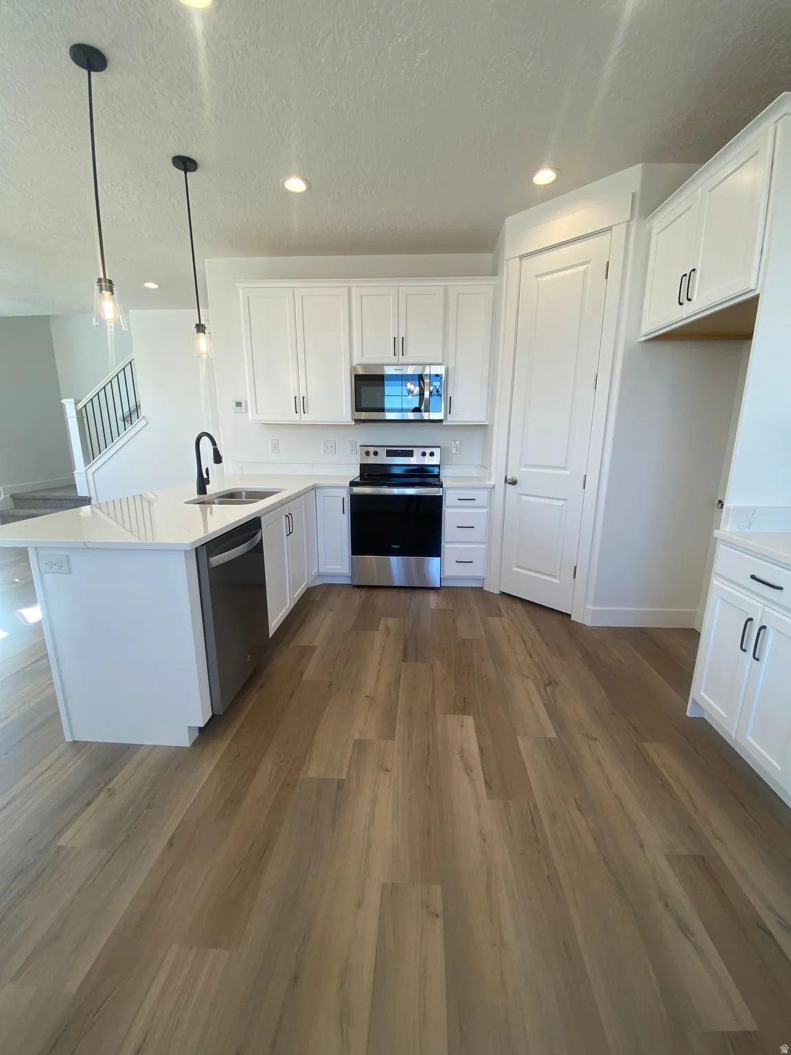 Kitchen with white cabinets, stainless steel appliances, a textured ceiling, a peninsula, and pendant lighting*Photos are for reference only and are not of specific unit listed.  Finishes may differ from pictures shown.