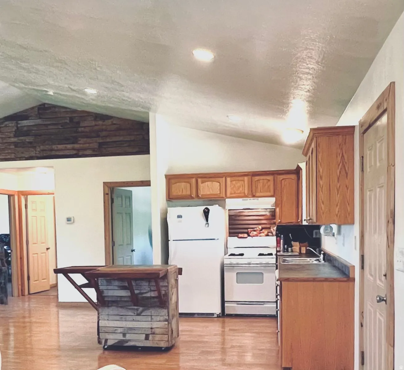 Kitchen with white appliances, wood finish cabinetry, light wood-type flooring, and dark countertops