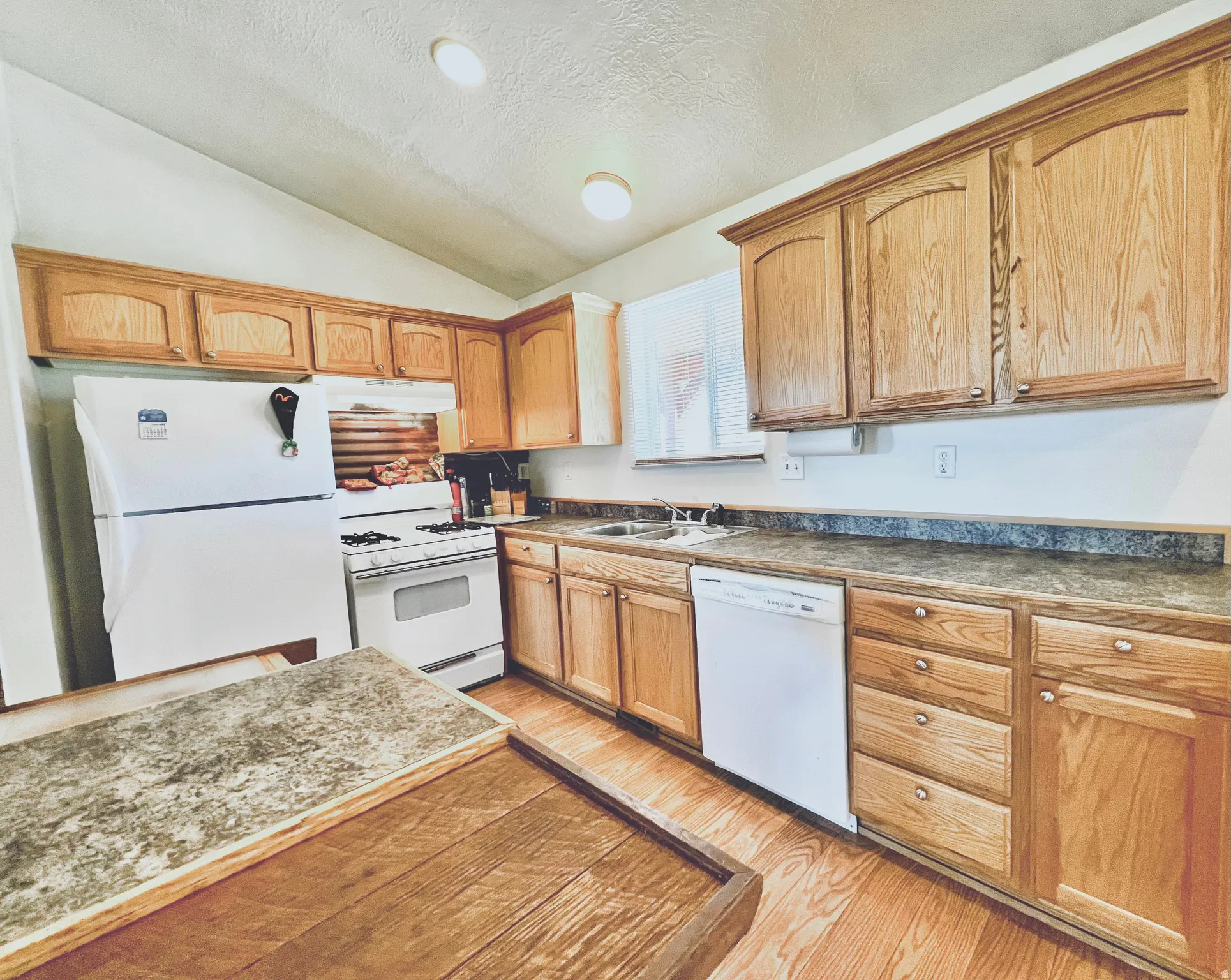 Kitchen featuring white appliances, dark countertops, light wood-type flooring, and wood finish cabinets