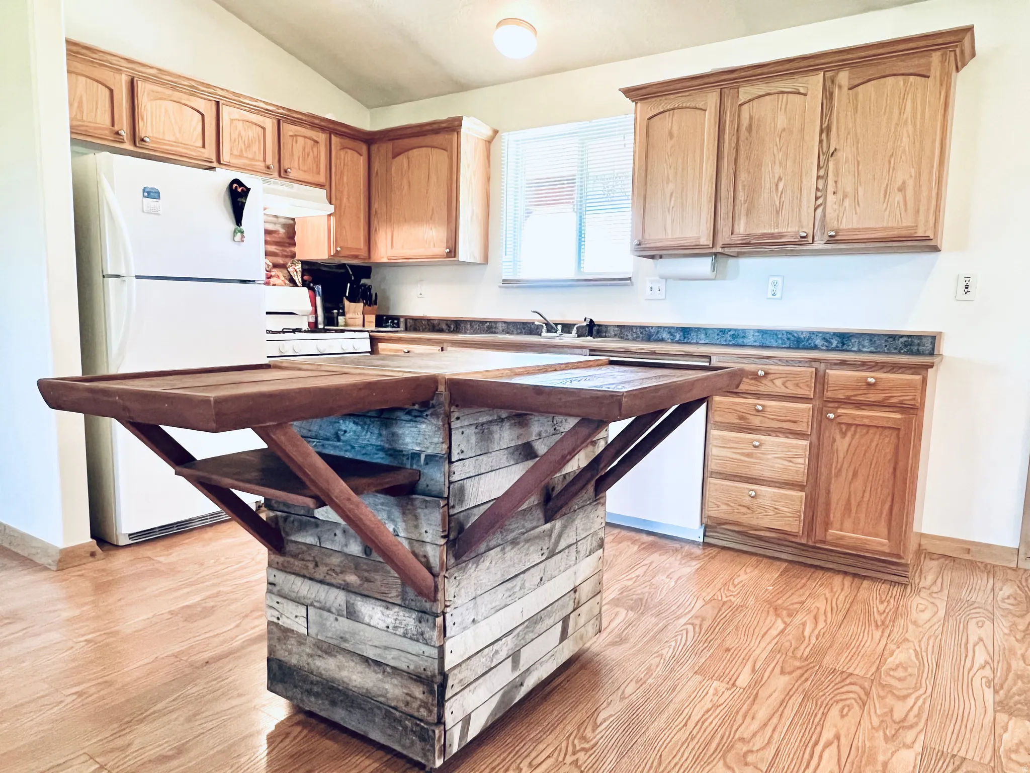 Kitchen featuring lofted ceiling, white appliances, light wood-style floors, and dark countertops