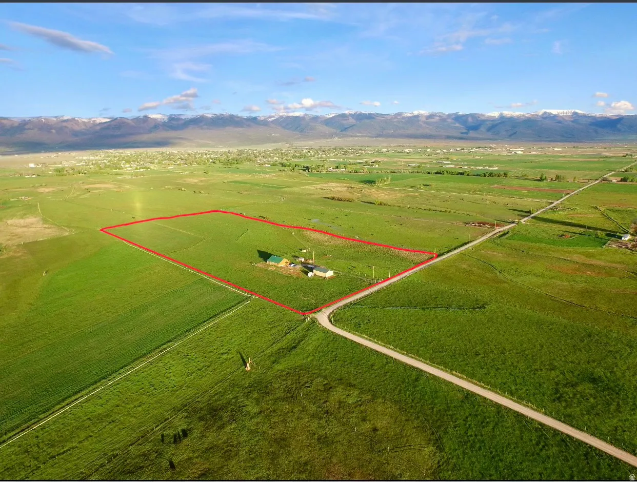 Expansive green acreage featuring a primary residence with a green roof, outbuildings, and a gravel road leading to the property