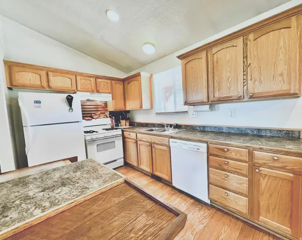 Kitchen featuring white appliances, dark countertops, light wood-type flooring, and wood finish cabinets