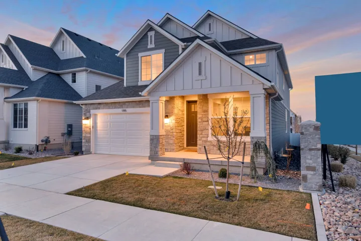 View of front of property featuring board and batten siding, driveway, a yard, and stone siding