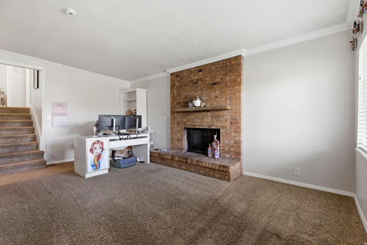 Unfurnished living room featuring a brick fireplace, carpet floors, ornamental molding, a textured ceiling, and a desk