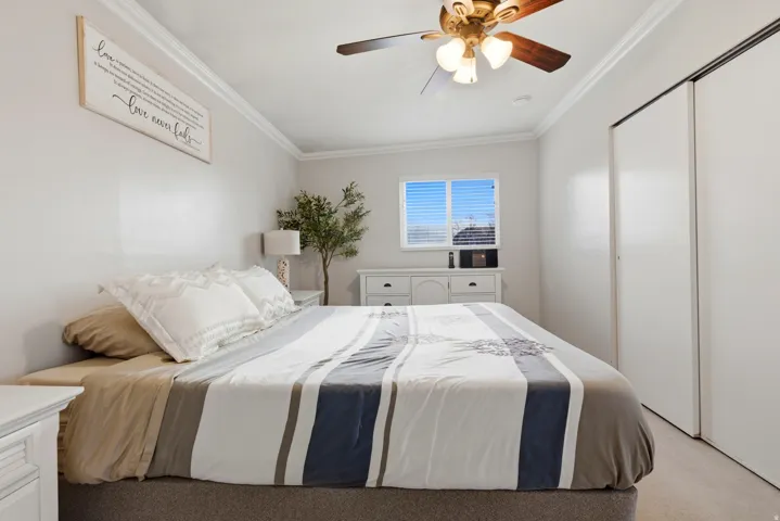 Bedroom with ornamental molding, a ceiling fan, a closet, and light carpet