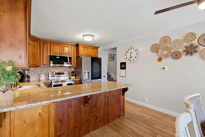 Kitchen with wood finish cabinetry, stainless steel appliances, ornamental molding, a ceiling fan, and light stone countertops