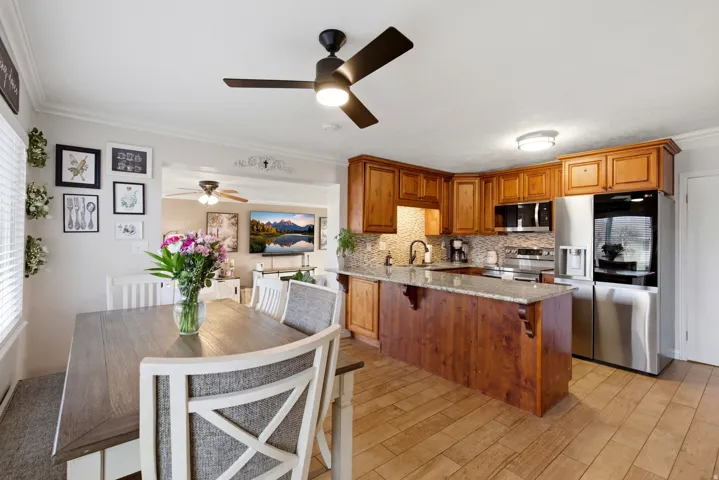 Kitchen featuring wood finish cabinets, light stone countertops, stainless steel appliances, a peninsula, and ornamental molding